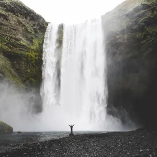 A huge waterfall in the background and a small figure standing at the bottom, raising their arms.