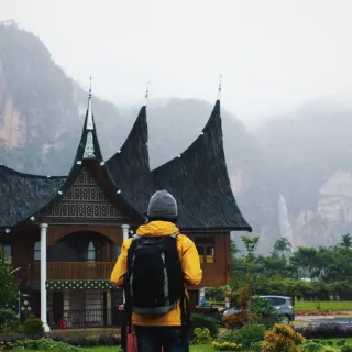 A hiker stands in front of an old asian building. Misty mountains in the background.